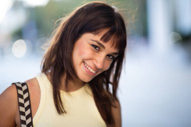 Şehirde dikilmiş, kameraya bakıp gülümseyen güzel bir genç kadının portresini yakından çek.