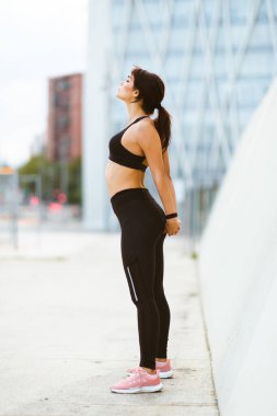 Dışarıda duran ve esneme egzersizi yapan sağlıklı bir genç kadının tam boy yan portresi.