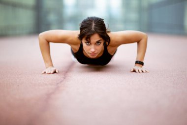 Beton zeminde şınav çeken güçlü genç bir kadının düşük açılı portresi.