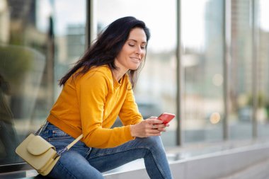 Şehrin dışında oturan beyaz bir kadın cep telefonu kullanıyor.