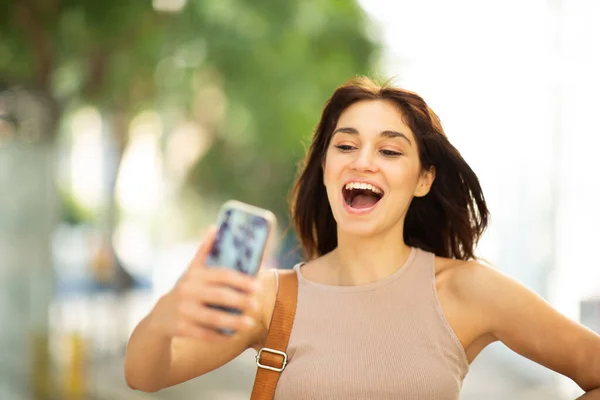 街の外で彼女の携帯電話で自慰行為をする陽気な若い女性の肖像画を閉じます — ストック写真