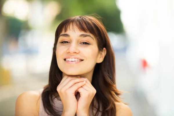 Close up portrait of beautiful young woman with hands under her chin looking at camera outside