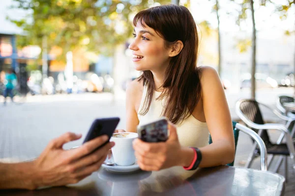 美丽的年轻女子与朋友坐在户外咖啡馆里拿着电话的画像 — 图库照片