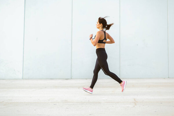 Full body side portrait of sportswoman jogging outdoors in morning