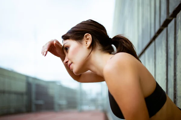 Close up side portrait of exhausted woman resting after workout session wiping sweat from her forehead