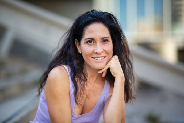 Улыбающаяся взрослая женщина в майке танка позирует с рукой на подбородке