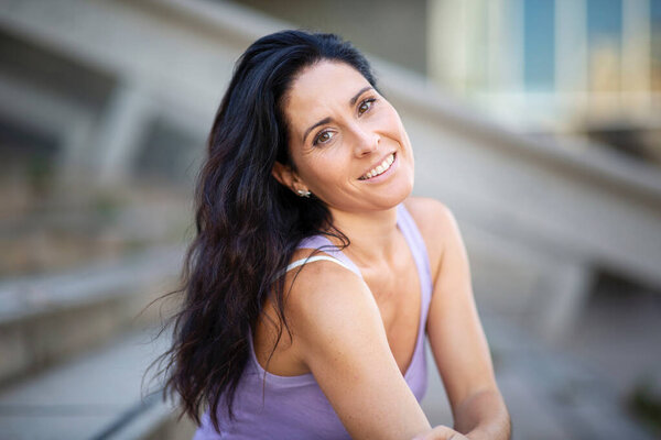 Портрет улыбающейся модели в майке-цистерне и длинные волосы, позирующие на открытом воздухе в городе