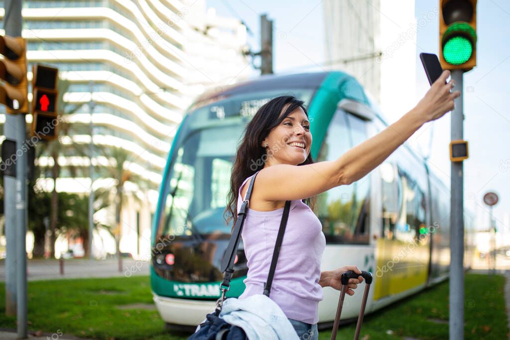 Happy woman traveler taking selfie using mobile phone in front of city tram