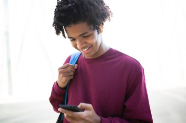 Gülümseyen genç adam dışarıda akıllı telefon kullanarak mesaj atıyor.