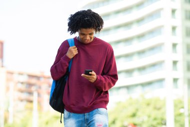 Mutlu Afro-Amerikan adam açık havada akıllı telefon kullanarak mesajlaşıyor.