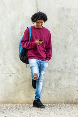 Mutlu Afro-Amerikalı adam dışarıda duvara yaslanırken cep telefonuyla mesaj atıyor.