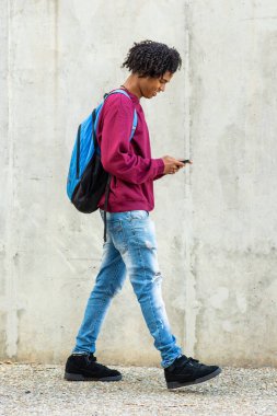 Şehirde yürürken cep telefonu kullanan sırt çantalı mutlu bir adam.