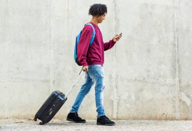 Şehirde bavulu dışarı çekerken cep telefonu kullanan mutlu siyah adam.