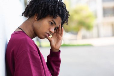 Genç Afro-Amerikan bir adam duvara yaslanıyor ve kafasını kaldırmadan bakıyor.