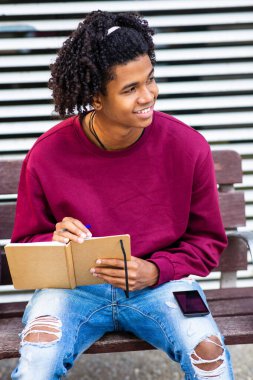 Mutlu Afro-Amerikalı adam dışarıda cep telefonu ve not defteriyle otururken gözlerini kaçırıyor.