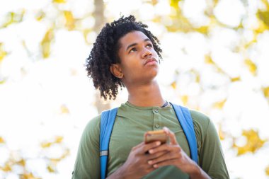 Genç adam dışarıda cep telefonu kullanırken yukarı bakıyor.