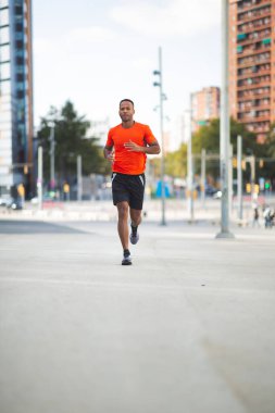 Spor giyimli Afro-Amerikan bir adam şehir sokaklarında koşuyor.