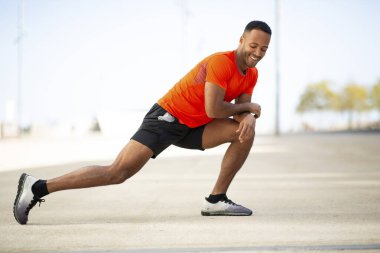 Mutlu bir adam şehirde koşmadan önce bacaklarını açıp ısınıyor.