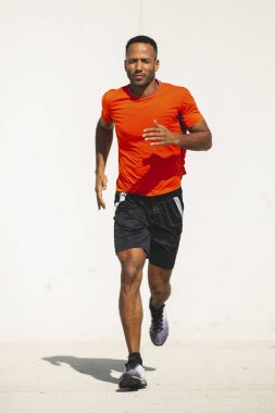 Parlak güneşli bir günde spor kıyafetli genç adam açık havada koşuyor.