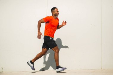 Parlak güneşli bir günde spor kıyafetli bir adam dışarıda koşuyor.