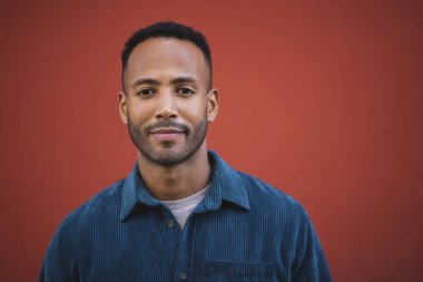 Yakışıklı Afrikalı Amerikalı adam, kestane rengi arka planda gülümsüyor.