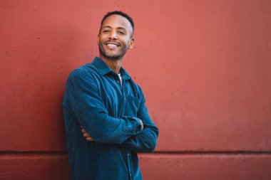 Kollarını kestane rengi duvara dayayıp başka tarafa bakan neşeli genç adam.