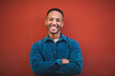 Kestane rengi arka planda kollarını kavuşturmuş genç bir adamın portresi.