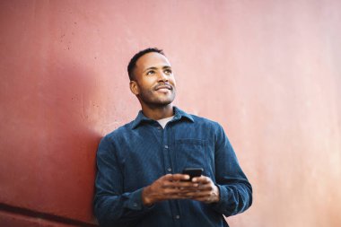 Afrika kökenli Amerikalı bir adam cep telefonuyla dışarıdaki duvara bakıyor.