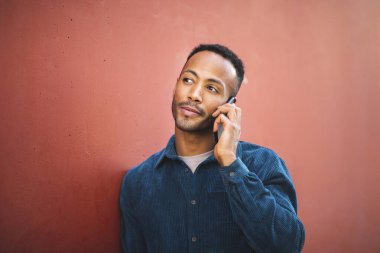 Duvara yaslanan ve cep telefonuyla konuşan Afrikalı genç bir Amerikalı.