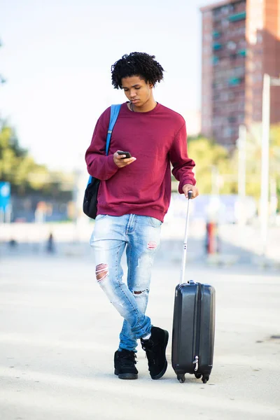 African american man with luggage messaging using mobile phone outdoors in city