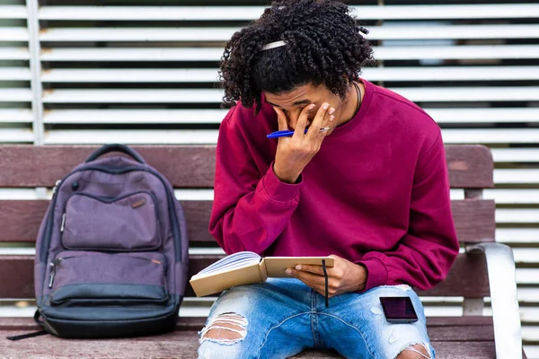 Man sitting outside and rubbing his eyes while writing in book