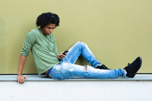 Uomo Afroamericano Messaggistica Utilizzando Smart Phone Mentre Seduto Sul Muro — Foto Stock