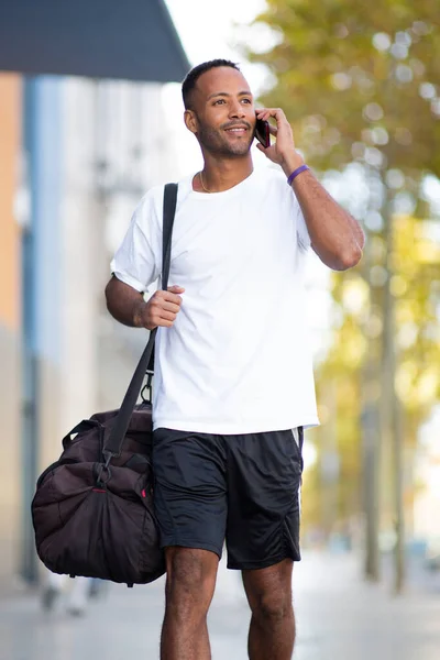 Mężczyzna Rozmawia Przez Telefon Komórkowy Podczas Noszenia Torby Sportowej Zewnątrz — Zdjęcie stockowe