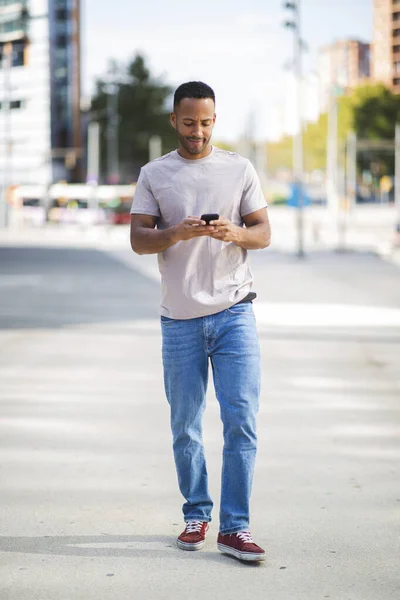 アフリカ系アメリカ人の男性が屋外で携帯電話を使用してテキストメッセージ — ストック写真