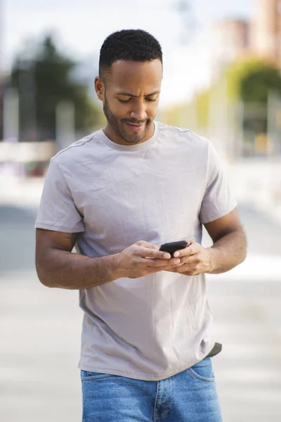 アフリカ系アメリカ人の男性が市内の屋外でスマートフォンを使ってテキストメッセージ — ストック写真