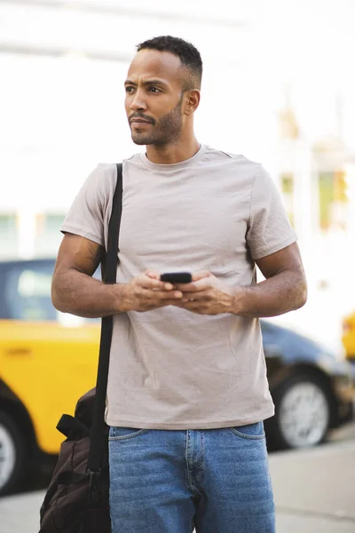 Przystojny Afroamerykanin Odwraca Wzrok Telefonem Komórkowym Torbą Mieście — Zdjęcie stockowe