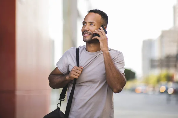 Happy young man with bag talking on mobile phone outdoors in city