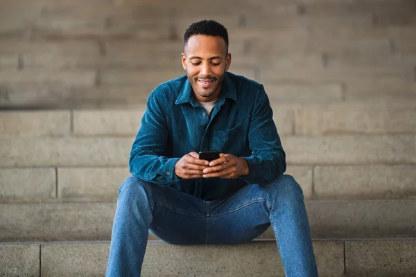 Happy man messaging using mobile phone outdoors on stairs