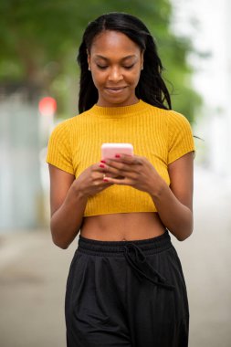 Gülümseyen Afro-Amerikan kadın açık havada cep telefonuyla mesajlaşıyor.