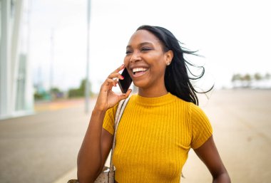 Neşeli Afro-Amerikalı kadın şehir dışında akıllı telefondan konuşuyor.