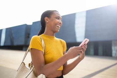 Neşeli Afro-Amerikalı kadın dışarıda akıllı telefon kullanırken gülüyor.