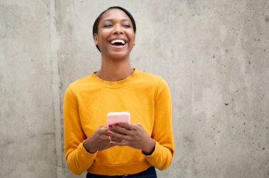 Neşeli siyah kadın dışarıda cep telefonu kullanırken gülüyor.