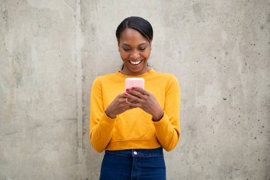 Neşeli Afrikalı Amerikalı kadın cep telefonuyla mesaj atıyor.