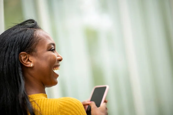 Over the shoulder shot of woman looking away and laughing while using mobile phone