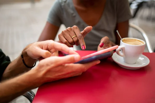 Diverse man and woman sharing smart phone content at outdoor coffee shop