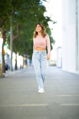 Sokakta yürüyen mutlu genç bir kadının tam boy portresi.
