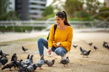 Açık hava parkında güvercinleri besleyen mutlu genç kadın portresi.