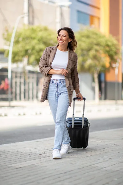 城市里快乐的年轻女旅行家拉着手提箱的全身像 — 图库照片