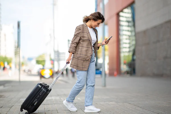 Full length side portrait of woman walking with suitcase and mobile phone