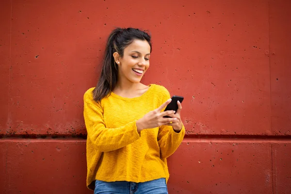 Портрет Улыбающейся Молодой Женщины Стоящей Красной Стены Смотрящей Мобильный Телефон — стоковое фото